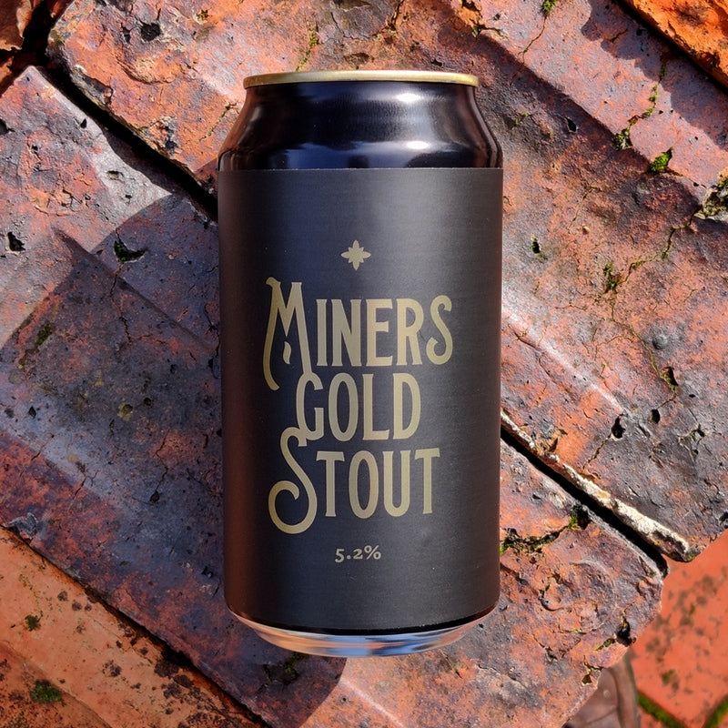 This is a photo of a can of Miners Gold Stout that is layed down on some bricks for the photo.